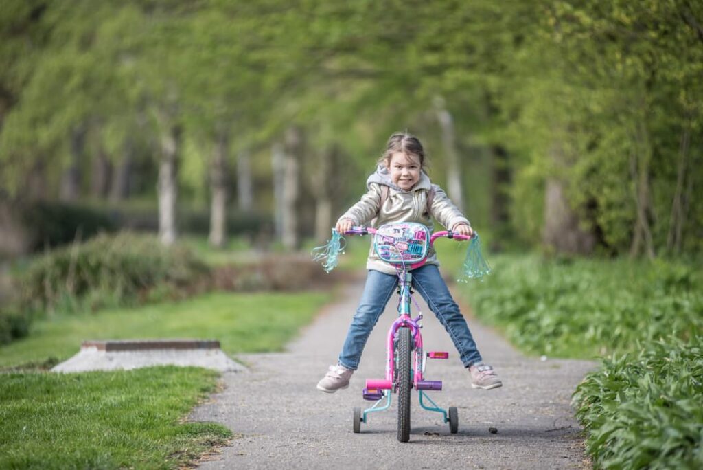 Fille qui apprends à faire du vélo rose petite roue dans un parc